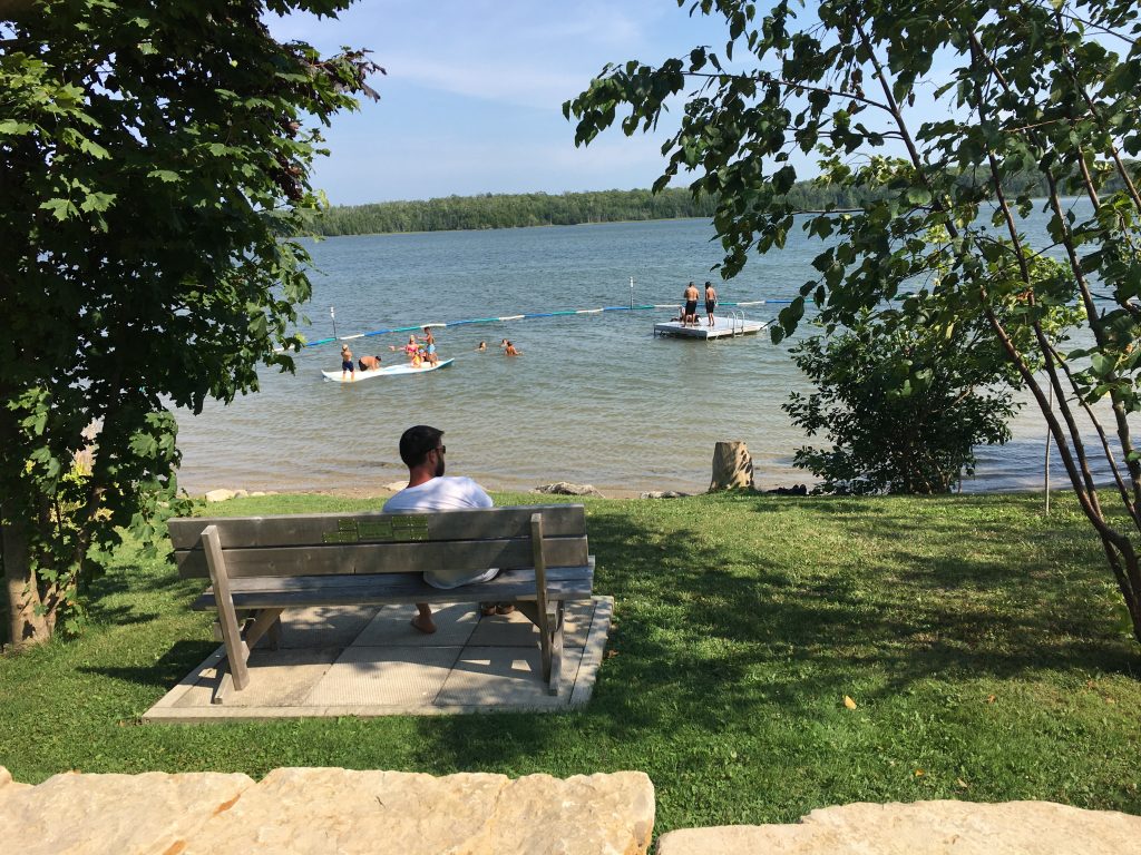 person sitting on a bench looking over Miller Lake with people playing in the water